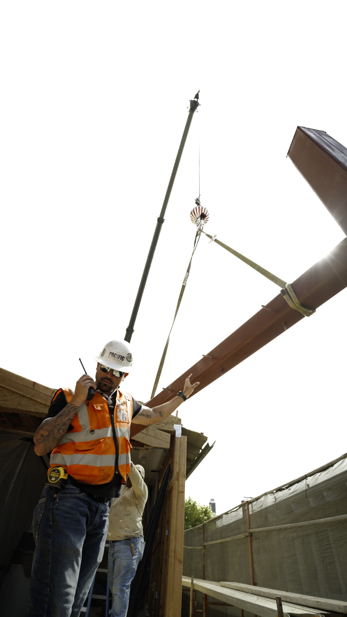 Construction worker using a radio to coordinate a steel beam crane lift